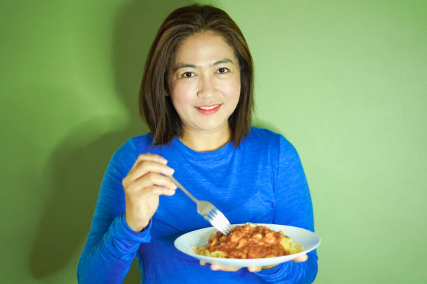 Portrait Women eating spaghetti on green wall.