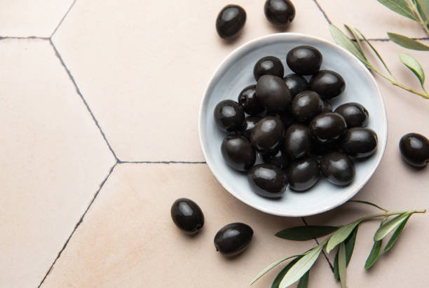 istock Black olives served in ceramic bowl on hexagonal beige tiles, decorated with olive tree branch 2199294373