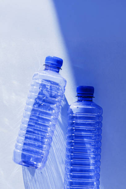istock Blue plastic water bottles on white blue background with sunlight shadow and sun flare, Minimal top view photo, themes of ecology, recycling, sustainable living, reduce disposable plastics 2199301487