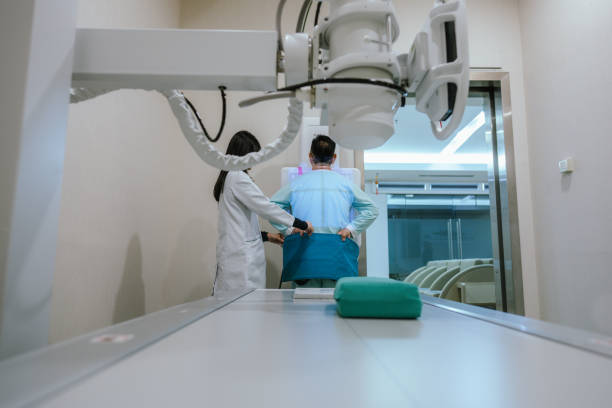 A young Asian female radiologist adjusting the machine for an adult man undergoing a digital chest X-ray examination at the hospital.