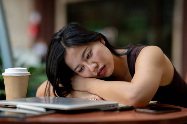 A sad, tired Asian woman lays her face down on the table outdoors, feeling exhausted from work.
