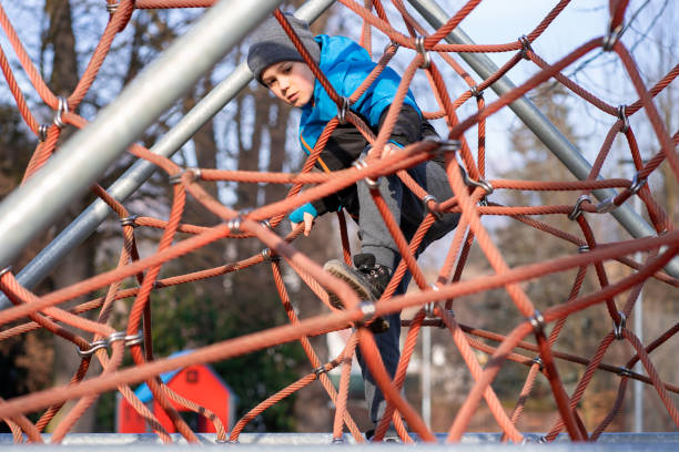 A child climbs up an alpine grid in a park on a playground on spring day.