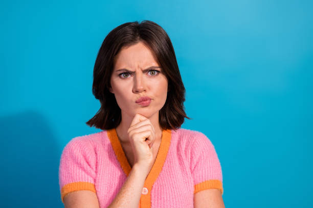 istock Thoughtful young woman with questioning expression against blue backdrop in casual pink vibrant attire 2199316242