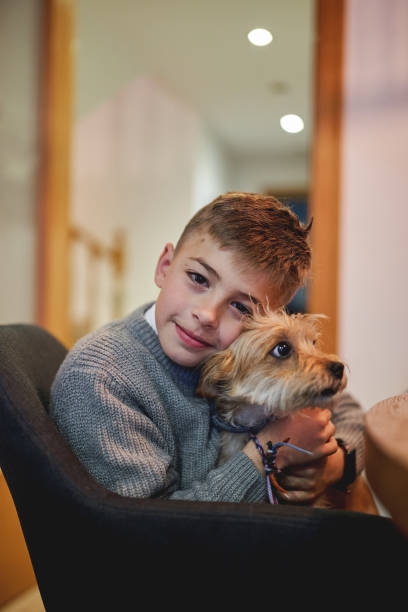 istock Smiling boy hugging his small dog while sitting on a chair at home 2199318115