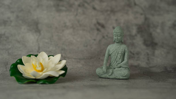 istock A statue of Buddha sits on a grey surface next to a white flower. The statue is sitting in a lotus position, and the flower is placed in front of it. Concept of peace and tranquility 2199320619