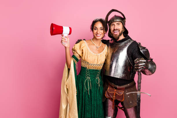 istock Couple in medieval-themed costumes posing in a modern setting with a pink background. 2199322687