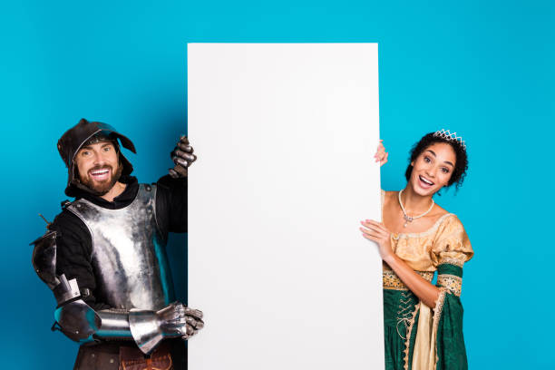 istock Medieval couple in themed costumes posing with blank board over vibrant pink backdrop 2199322773