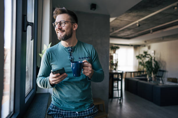 istock Smiling man enjoying morning coffee and checking his smartphone by the window 2199323347