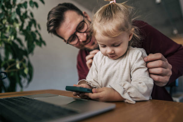 istock Father and daughter using smartphone and laptop at home 2199325154