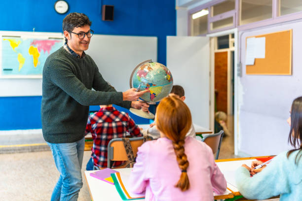 istock Teacher pointing at globe in geography lesson with elementary students 2199327879