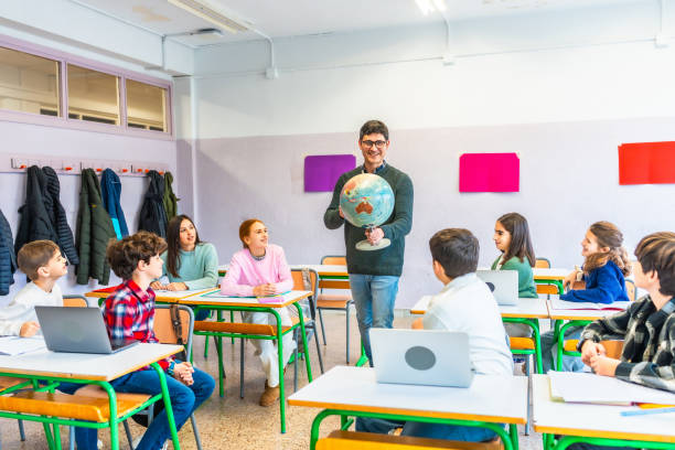 istock Geography teacher holding globe, teaching students in classroom 2199327909