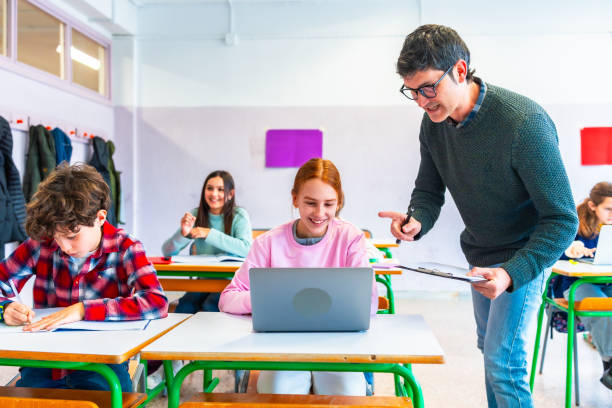 istock Teacher helping students studying with laptop in classroom at school 2199327988