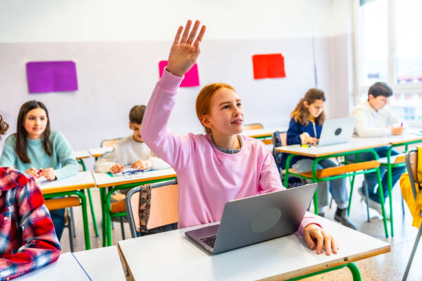 Teenage student raising hand in classroom with laptop