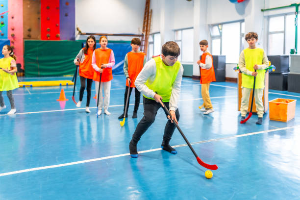 Group of elementary age children playing floorball in school gym class, learning teamwork and hand-eye coordination