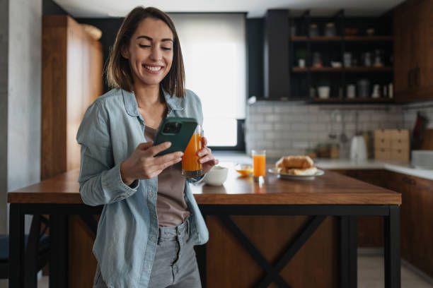istock Young woman enjoying breakfast and using smartphone in modern kitchen 2199329624