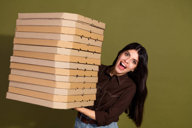 istock Cheerful woman holding pizza boxes on a khaki background symbolizing delivery services 2199330071
