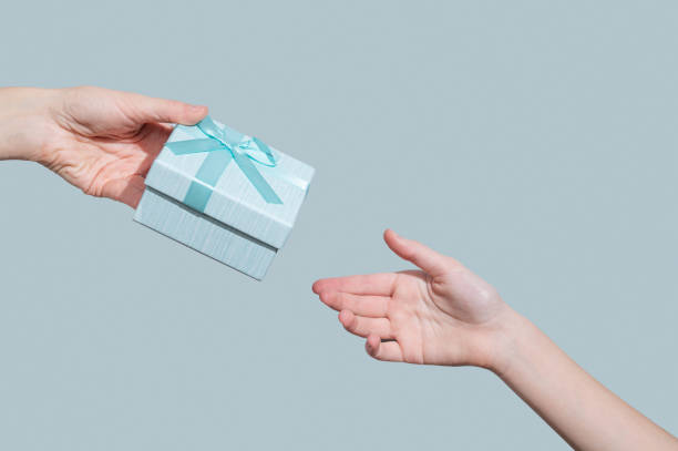 istock Hand with gift blue box reaching to another hand on light background. 2199335939
