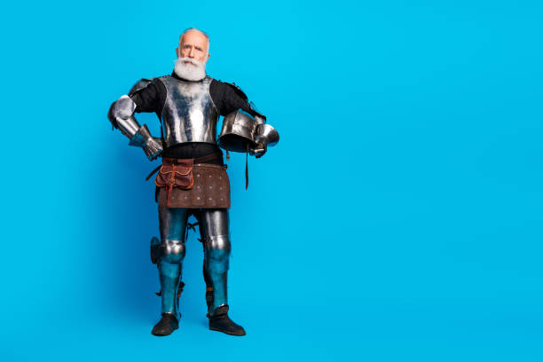 istock Senior man in medieval knight armor posing confidently against a bright blue background, demonstrating historic style 2199337234