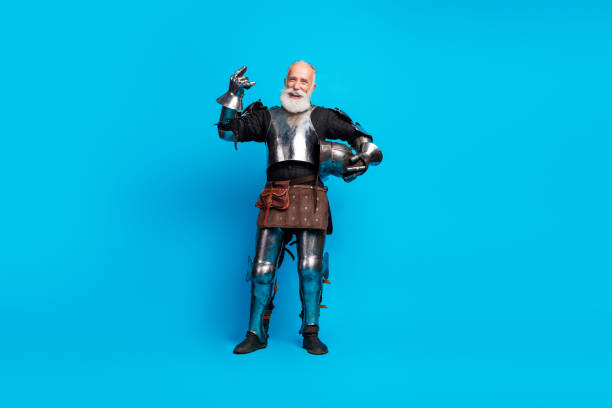 istock Elderly man in full knight armor striking a noble pose against a vibrant blue background, embodying medieval charm and history. 2199337278