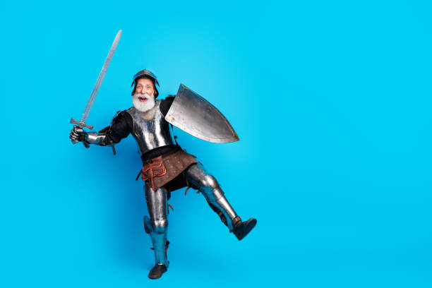 istock Cheerful retired knight posing in medieval armor with shield and sword against a bright blue background 2199337300