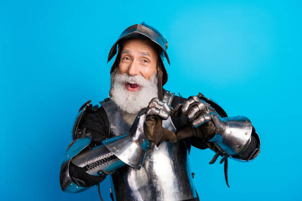 istock Charming senior man in medieval knight armor showing heart sign against blue background 2199337421