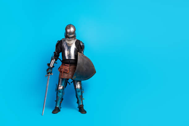 istock Medieval knight in full armor standing with sword and shield on vibrant blue background, historical and fairytale depiction 2199337439