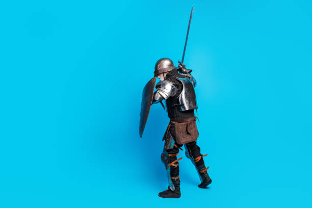 istock A medieval knight in metallic armor wielding a sword and shield against a vibrant blue background, exuding bravery and classic style. 2199337447