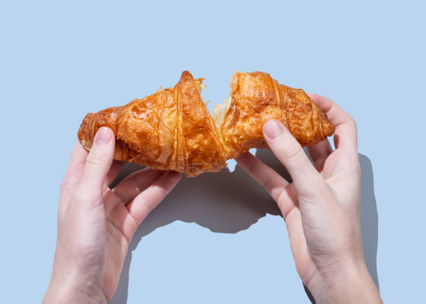 istock Hands breaking a fresh croissant over a blue background with shadow. Creative mockup for cafe 2199337697