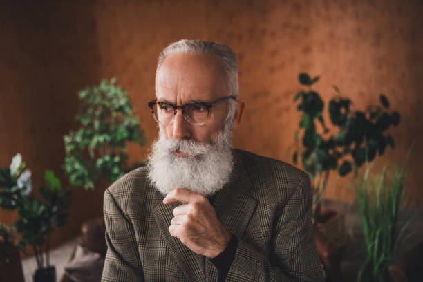 An elderly gentleman, showcasing refinement and elegance, wearing glasses and a fashionable suit, posed against a sophisticated retro-inspired backdrop featuring a vintage-style room.