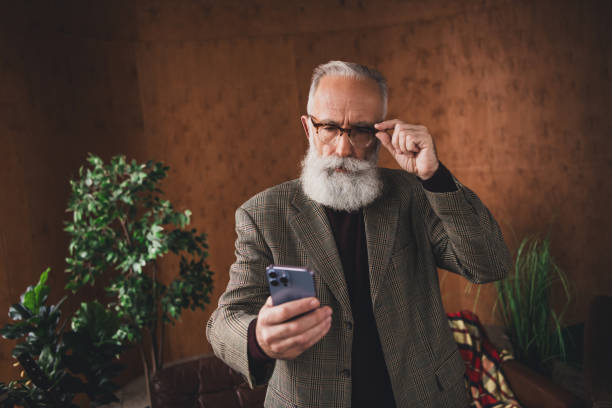 Stylish mature man with smartphone in retro interior holding glasses while standing near plants and embracing a nostalgic ambiance
