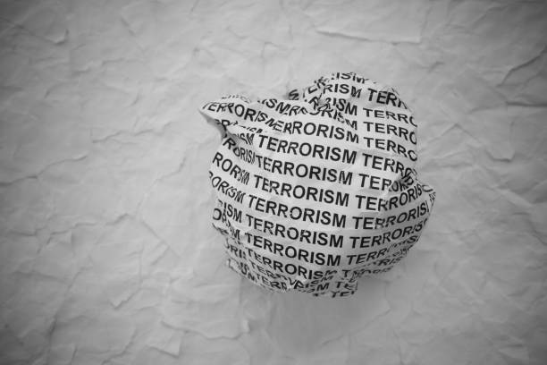 Crumpled paper ball with words Terrorism on torn white paper pieces background.