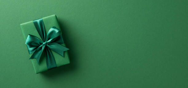 An elegant green gift box wrapped with satin ribbon, placed on a matching green background, perfect for celebrations and festive occasions