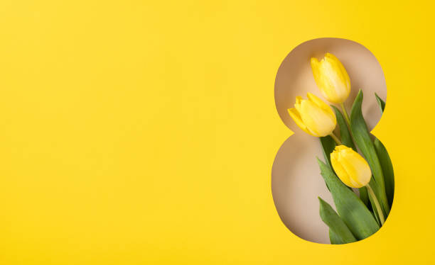 Bright yellow tulips arranged in a numeral eight cutout on a yellow backdrop, representing International Women's Day and spring themes