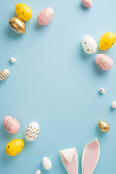 istock Decorative vertical Easter eggs in pastel shades and bunny ears arranged on a blue background 2199347802