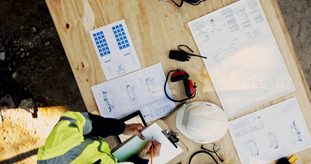 istock Blueprint, construction and person at table with layout, checklist and inspection paperwork from above. Architect, building project and contractor on site with floor plan, clipboard and safety gear 2199350998