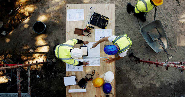 istock Blueprint, construction and men at table with planning, collaboration and site inspection paperwork from above. Architect, building team and contractor with layout, pointing and project management 2199351011