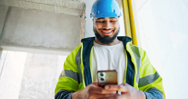 istock Man, phone and construction worker with texting, happy and contact with info for building development. Engineer, smartphone and smile with low angle, notification and click on mobile app at property 2199351102