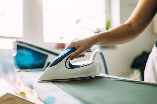 istock Person Ironing Clothes with a Modern Steam Iron in a Bright Room 2199352088
