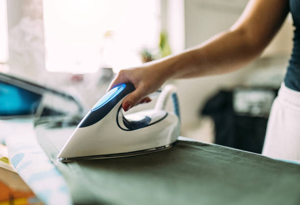 istock Person Ironing Clothes with a Modern Steam Iron in a Bright Room 2199352106