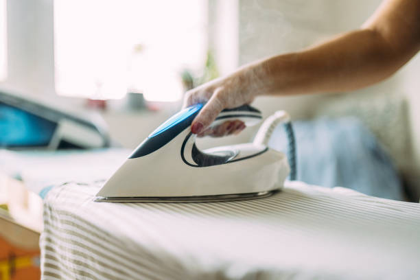 istock Person Ironing Clothes with a Modern Steam Iron in a Bright Room 2199352122