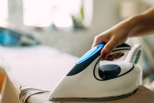 istock Person Ironing Clothes with a Modern Steam Iron in a Bright Room 2199352129