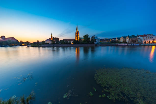 Wroclaw, Poland - July 25 2024: Historic Wroclaw Cathedral Spires Reflecting in Odra River at Sunset with Smooth Water Effect and Blue Hour Sky over Medieval Polish Cityscape
