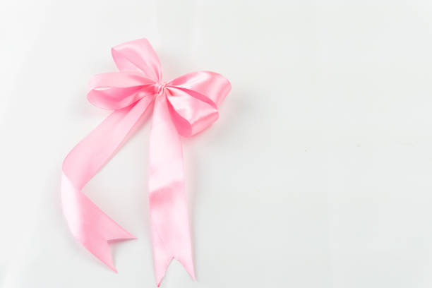 A delicate pink satin ribbon tied into a bow, gracefully resting against a pristine white backdrop. Perfect for gifts.