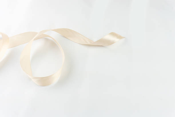 A single strand of soft, beige satin ribbon gently loops on a white backdrop, offering a sense of understated elegance.