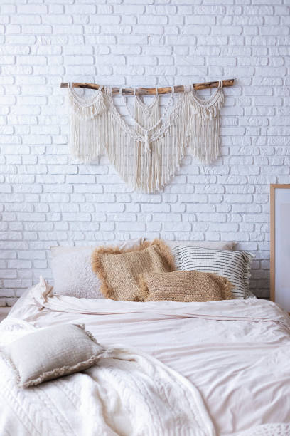 istock Cozy bedroom with interior design in boho style, bed mattress on floor, cushions, frame poster, home decor, stepladder, macrame panel against white brick wall. Concept of classy house and apartment. 2199359142