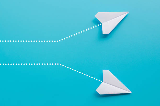istock Top view of 2 white paper airplane heading to different direction on blue background 2199360995