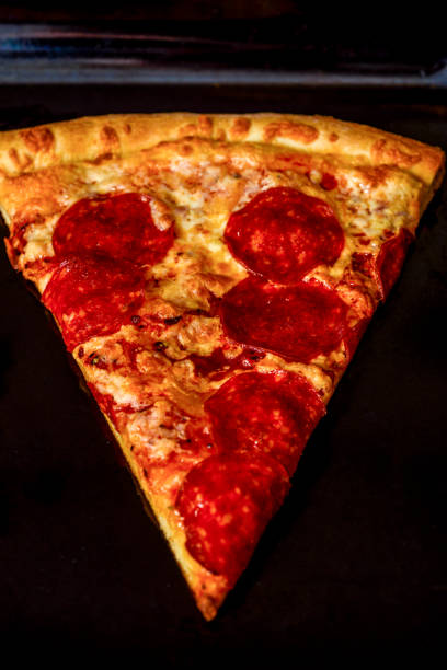 A slice of pizza on a black baking sheet in the oven. Fast food.