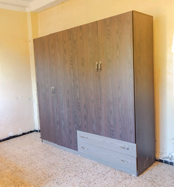 Two gray drawers, four doors and silver handles, in a room with granite tiled flooring and a deteriorated wall with black baseboard stained with paint.