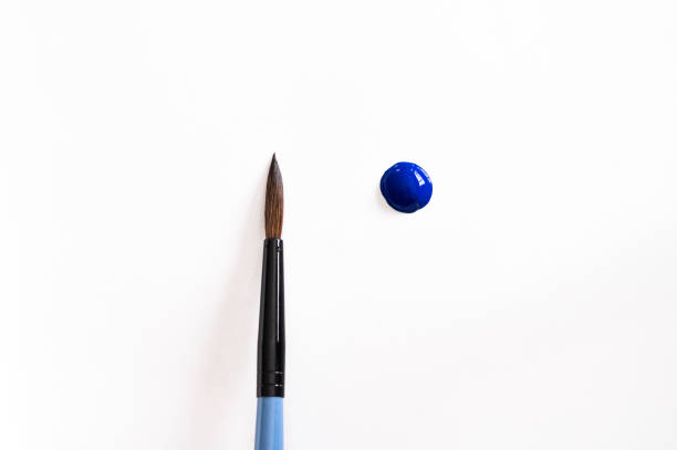A blue drop of paint next to a clean paintbrush on a white background