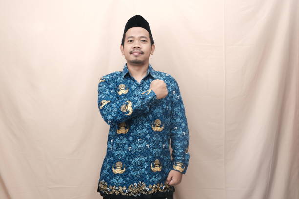 istock Confident Indonesian government worker man wearing  blue Korpri batik uniform with a raised fist gesture, symbolizing pride and determination. 2199370303